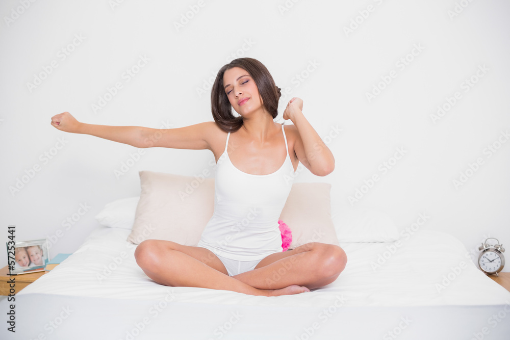 Relaxed young brown haired model in white pajamas stretching her Relaxed young brown haired model in white pajamas stretching her