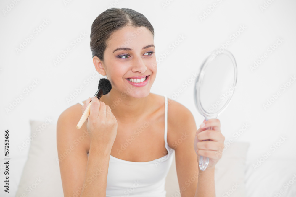 Smiling brown haired model in white pajamas applying powder on h Smiling brown haired model in white pajamas applying powder on h