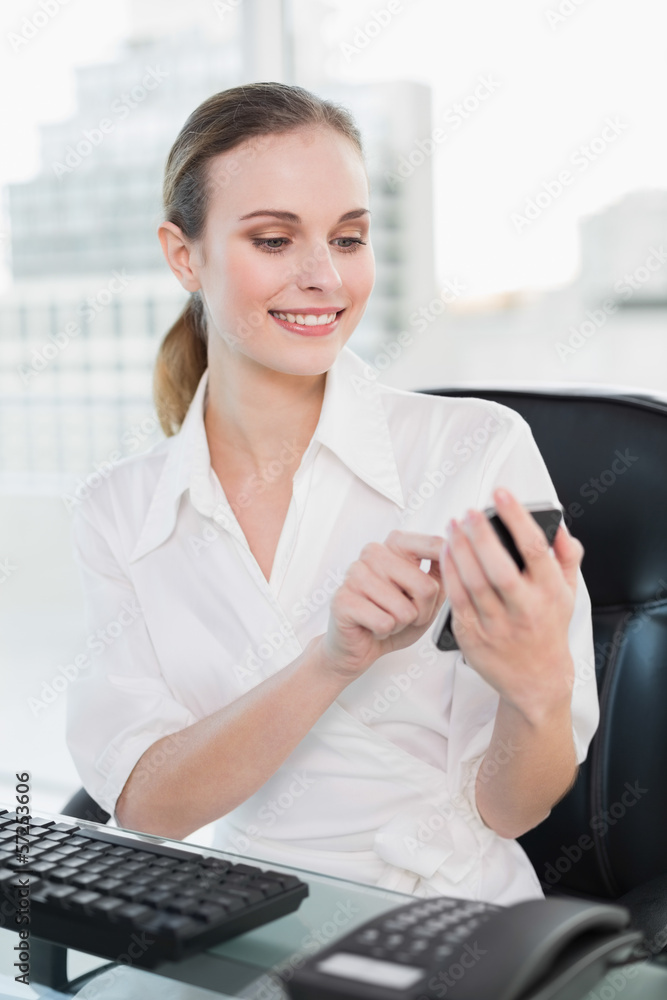 Happy businesswoman sitting at desk sending a text Happy businesswoman sitting at desk sending a text
