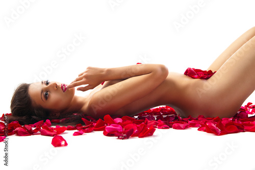 Fototapeta szczupła kobieta leży na płatkach czerwonych róż na białym