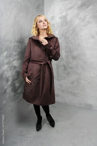 Beautiful young woman in purple coat standing in grey studio