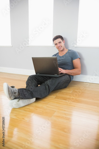 Content handsome man leaning against wall using laptop