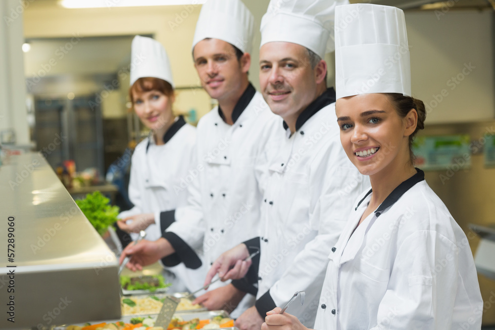 Four chefs smiling at camera while working at serving trays Four chefs smiling at camera while working at serving trays
