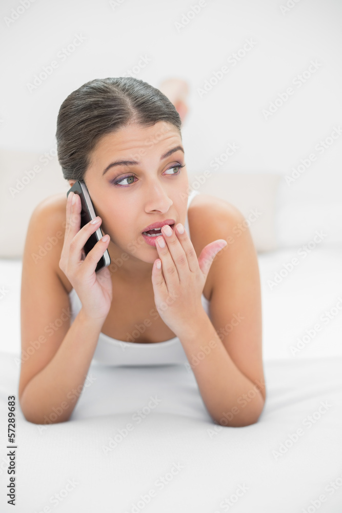 Shocked young brown haired model in white pajamas calling with h Shocked young brown haired model in white pajamas calling with h