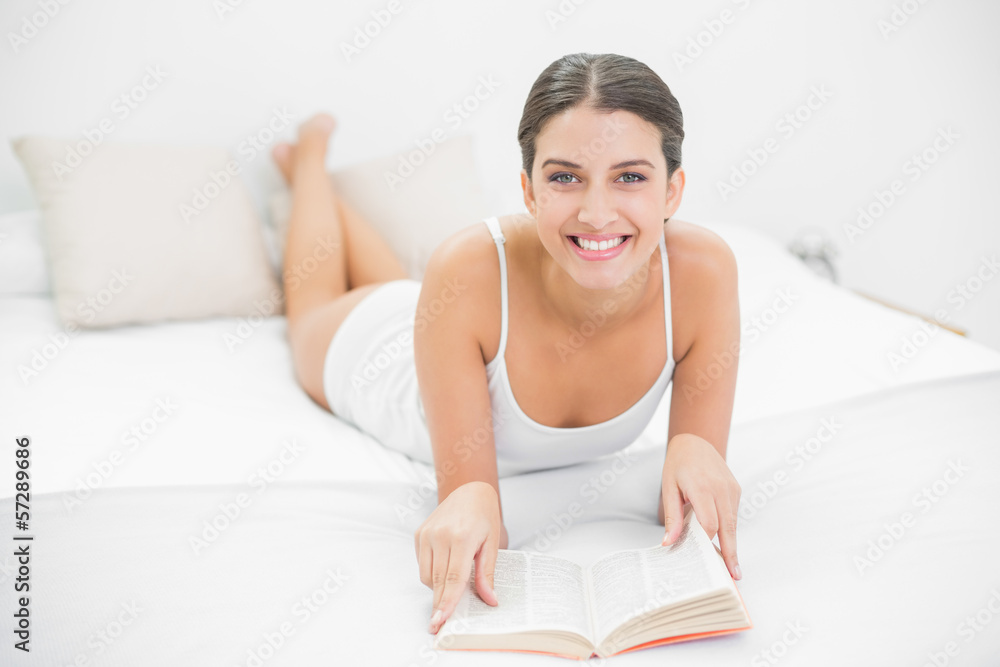 Delighted young brown haired model in white pajamas reading a bo Delighted young brown haired model in white pajamas reading a bo