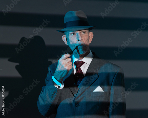 Retro detective man smoking pipe at night in office. Lit by ligh
