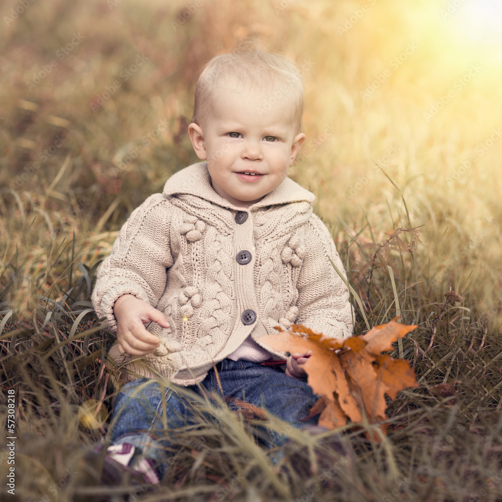 Playful child sitting on grass with maple leaves in fall season. Playful child sitting on grass with maple leaves in fall season.