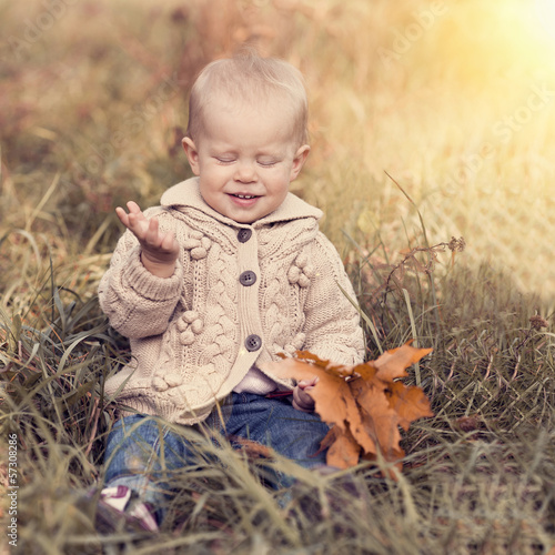 Beautiful blond kid playing with golden leaf on the nature