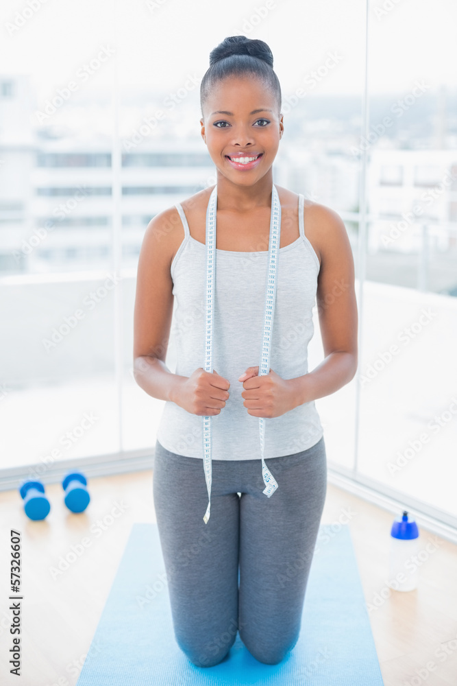 Smiling woman in sportswear holding measuring tape around her n