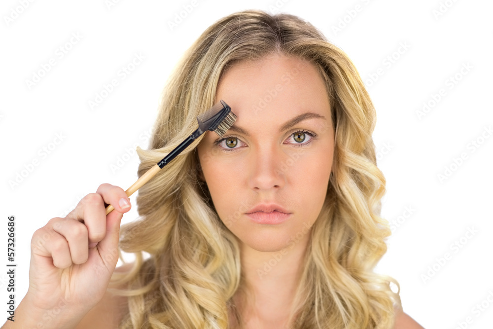 Serious curly haired blonde using eyebrow brush