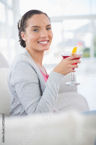 Happy woman sitting on sofa and holding cocktail