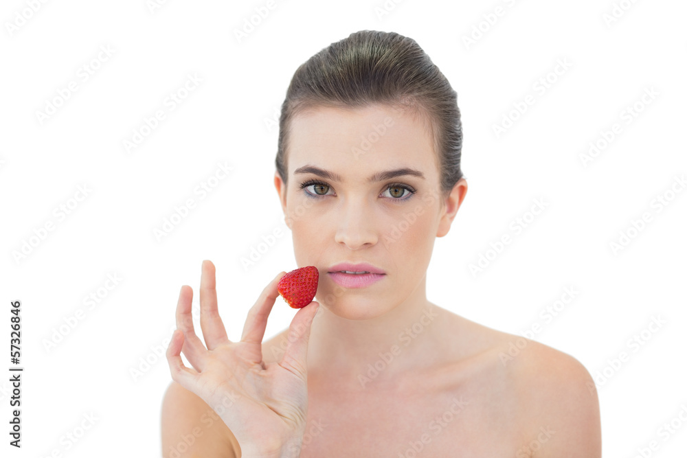 Serious natural brown haired model holding a strawberry Serious natural brown haired model holding a strawberry
