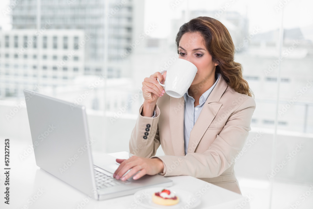 Businesswoman using laptop at her desk and drinking coffee Businesswoman using laptop at her desk and drinking coffee