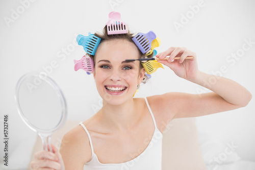 Happy natural brown haired woman in hair curlers brushing her ey