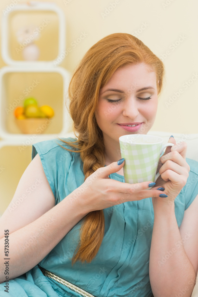 Smiling redhead sitting on the couch smelling coffee Smiling redhead sitting on the couch smelling coffee
