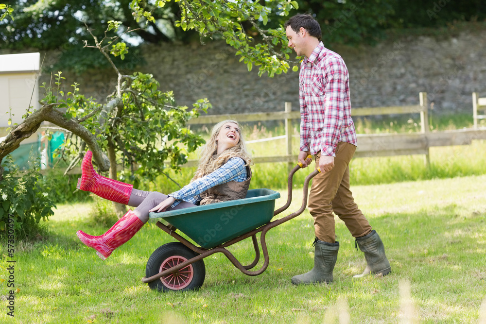 Handsome man pushing his laughing girlfriend in a wheelbarrow Handsome man pushing his laughing girlfriend in a wheelbarrow