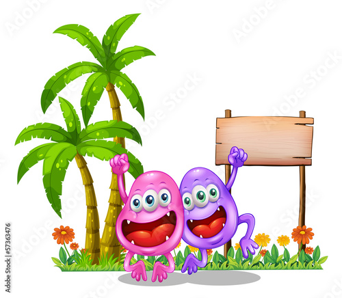 Two happy monsters near the empty wooden signboard beside the pa