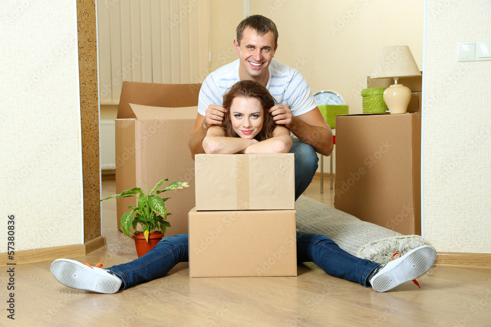 Young couple with boxes in new home on room background Young couple with boxes in new home on room background