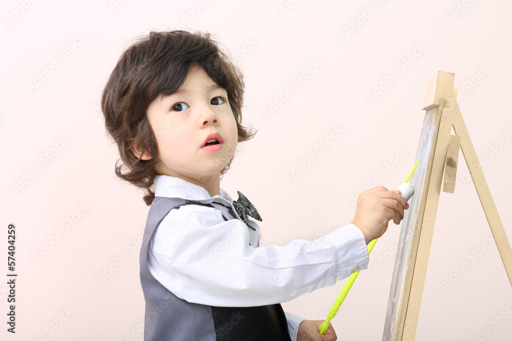 Little boy with yellow pointer draws with chalk on chalkboard