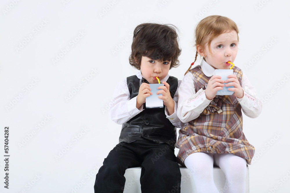 Little boy and girl sitting and drink juice on white background. Little boy and girl sitting and drink juice on white background.