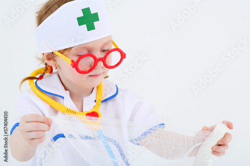 Little girl dressed as nurse spreads bandage on white photo