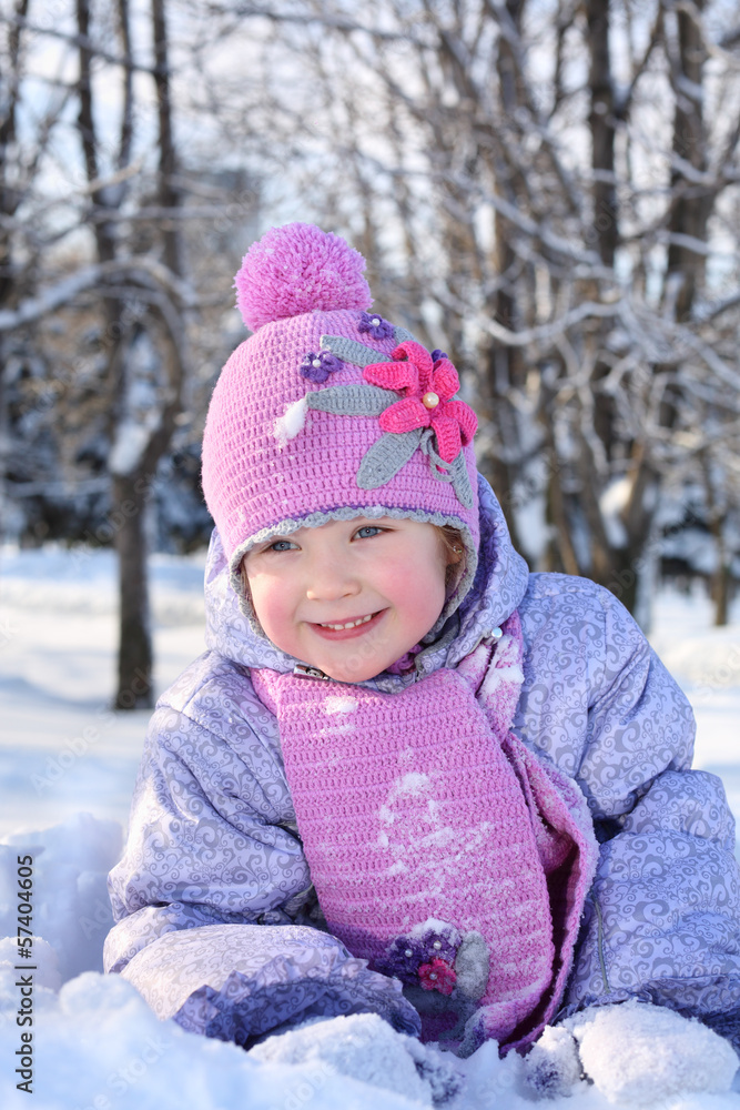 Happy little girl in pink scarf and hat lies in snow and looks Happy little girl in pink scarf and hat lies in snow and looks