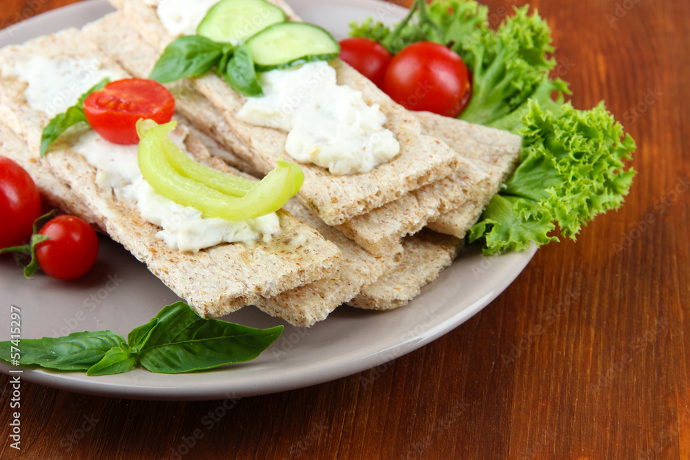 Tasty crispbreads with vegetables on wooden background