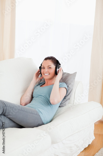 Charming female using headphones while lying on a sofa