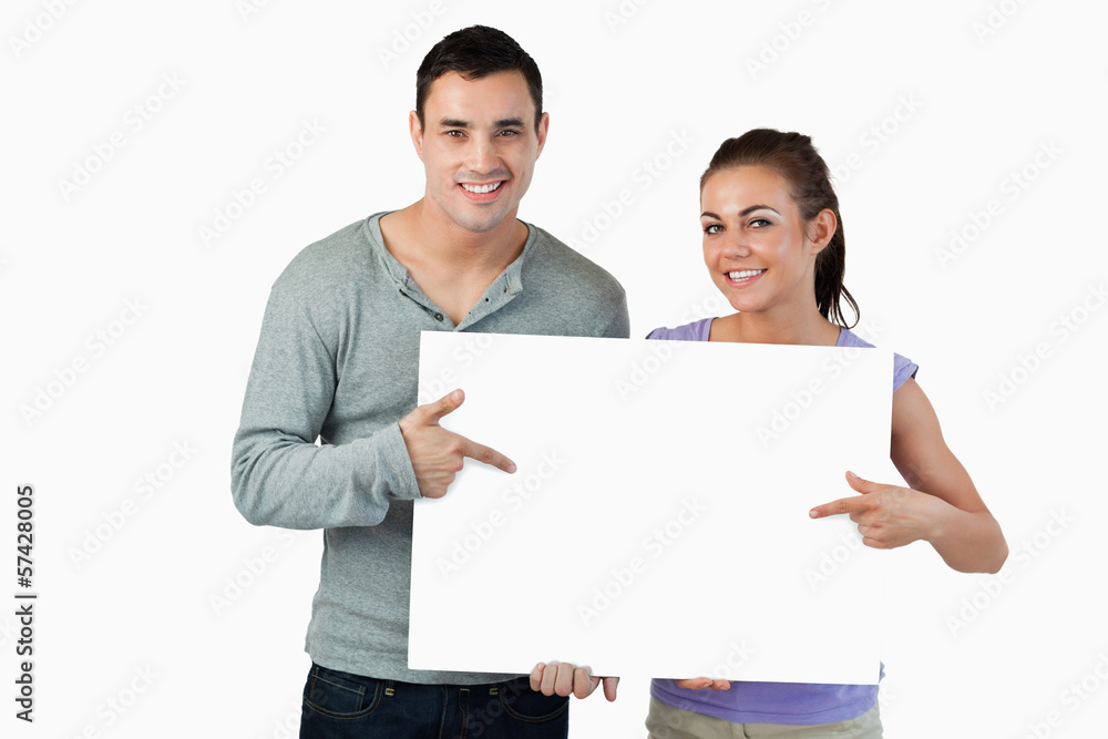 Smiling young couple pointing at sign they are holding Smiling young couple pointing at sign they are holding