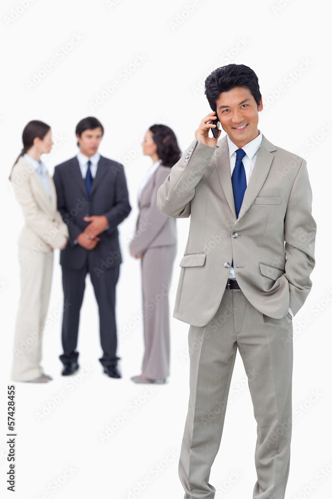 Businessman on cellphone with team behind him Businessman on cellphone with team behind him