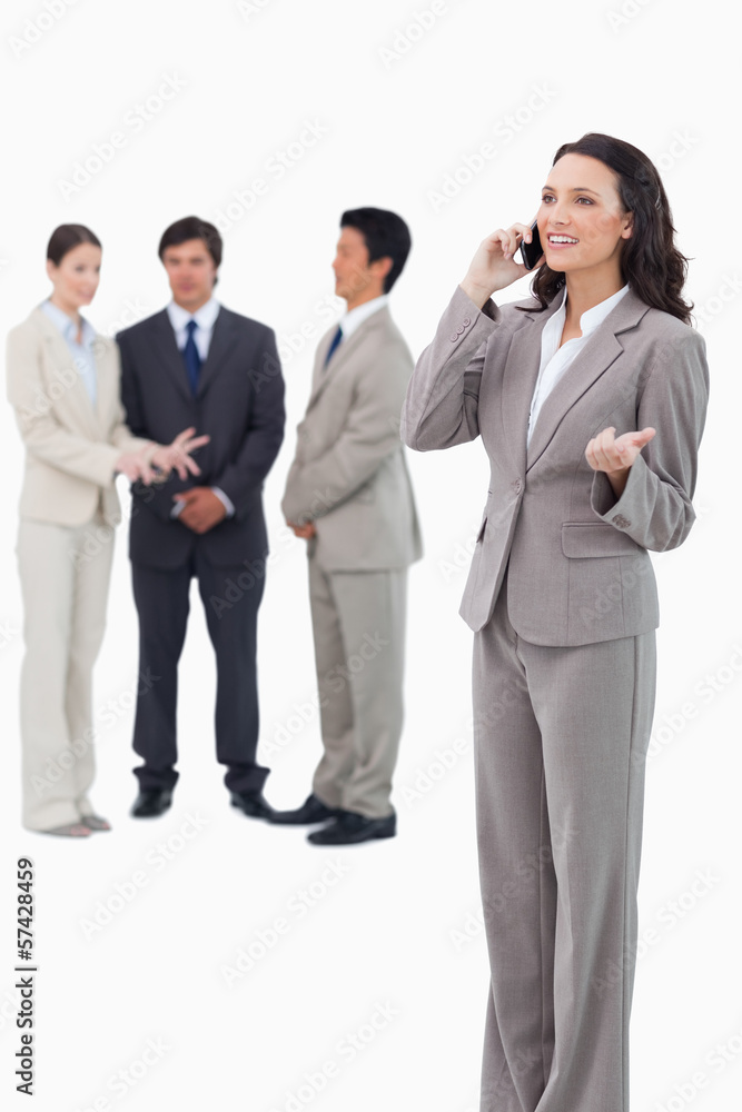 Saleswoman talking on cellphone with colleagues behind her Saleswoman talking on cellphone with colleagues behind her
