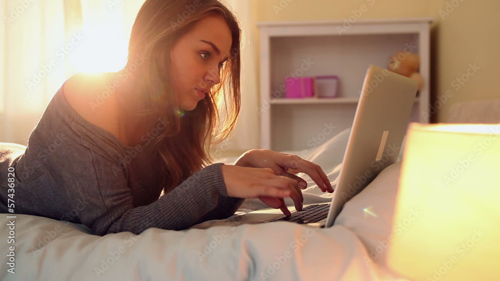 Pretty happy brunette lying on bed typing on laptop Pretty happy brunette lying on bed typing on laptop