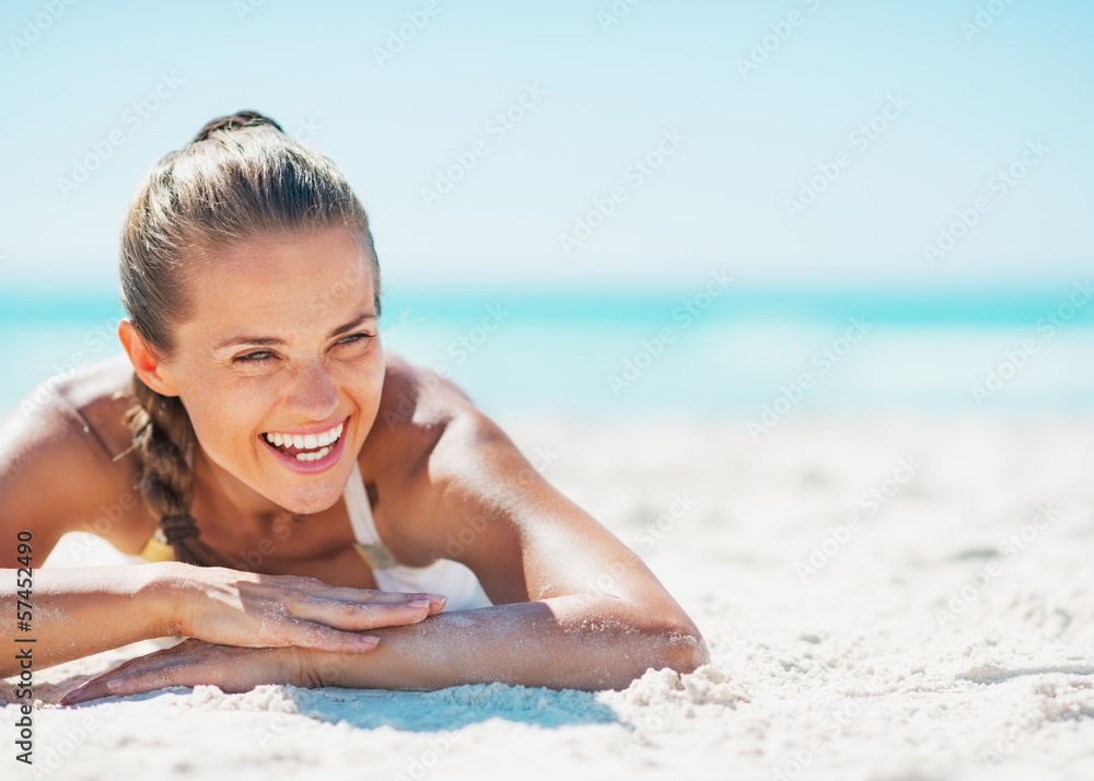 Smiling young woman in swimsuit enjoying laying on beach