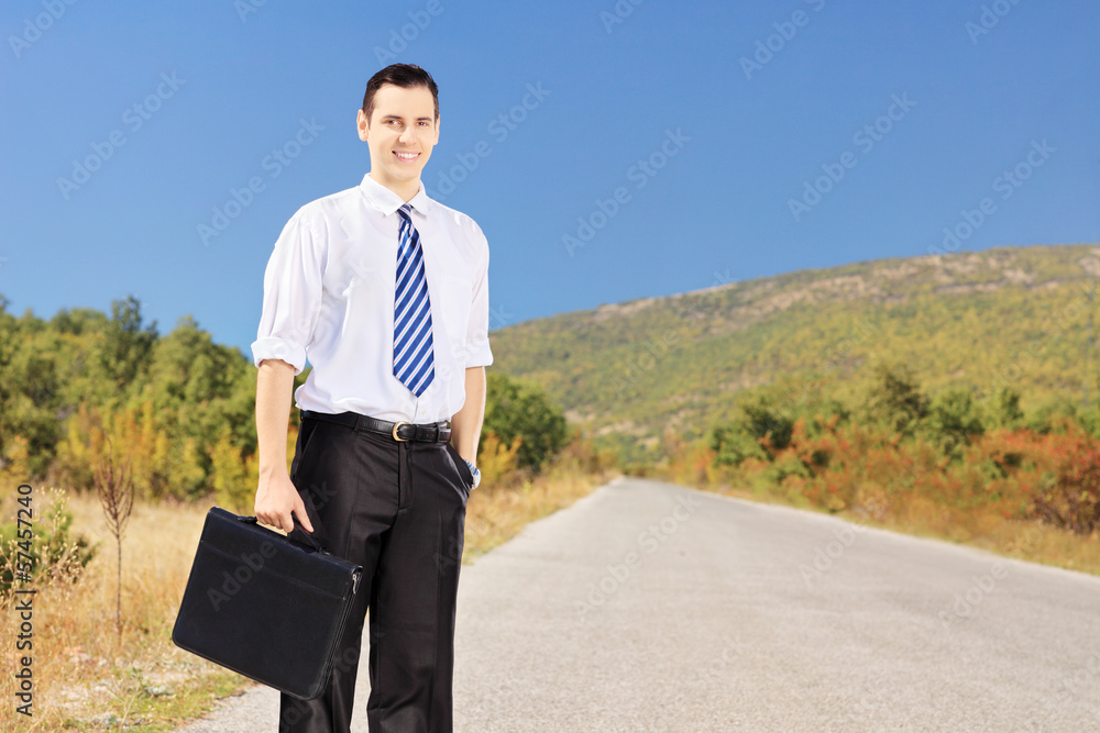 Young confident businessperson holding a suitcase on a road Young confident businessperson holding a suitcase on a road