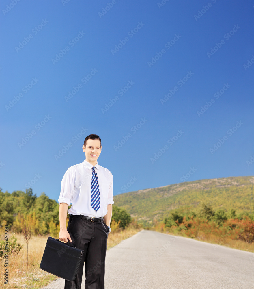 Young smiling businessperson holding a suitcase on a road Young smiling businessperson holding a suitcase on a road