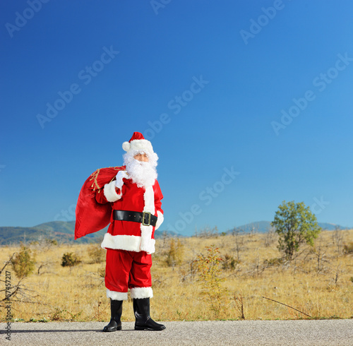 Full length portrait of a Santa claus with bag standing on a roa