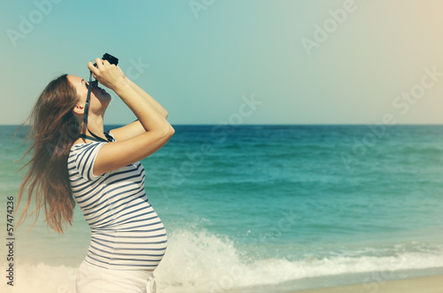 Young pregnant woman holding vintage camera. Photo in old color