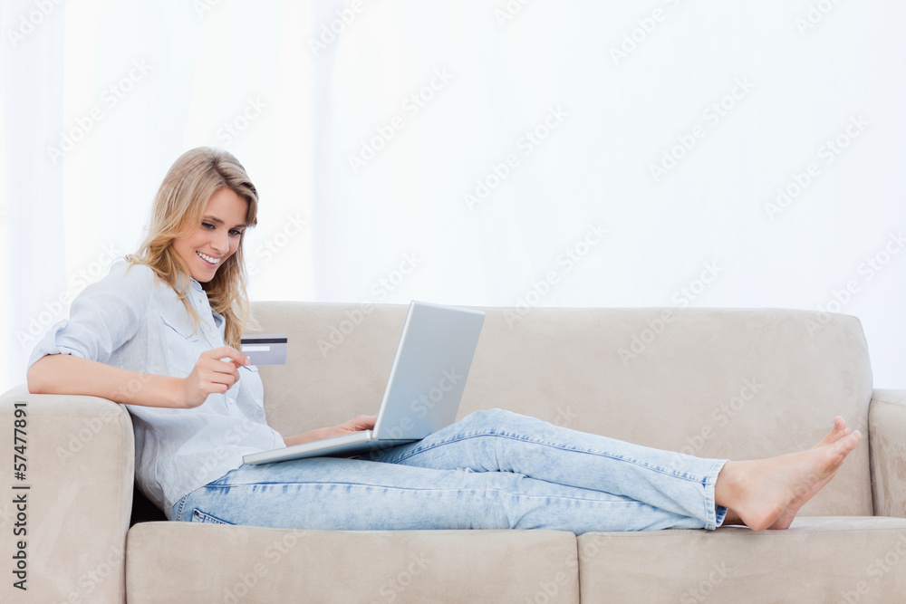 A woman lying on a couch with a laptop in front of her is holdin A woman lying on a couch with a laptop in front of her is holdin
