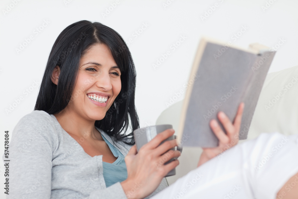 Woman smiling while holding a grey mug and a book Woman smiling while holding a grey mug and a book