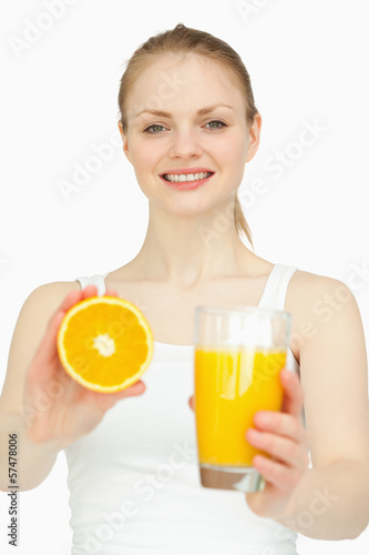 Smiling woman holding a glass while presenting an orange