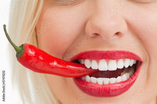 Smiling woman holding a chili with her teeth