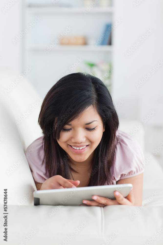 Smiling woman resting on a couch while playing with a tablet Smiling woman resting on a couch while playing with a tablet