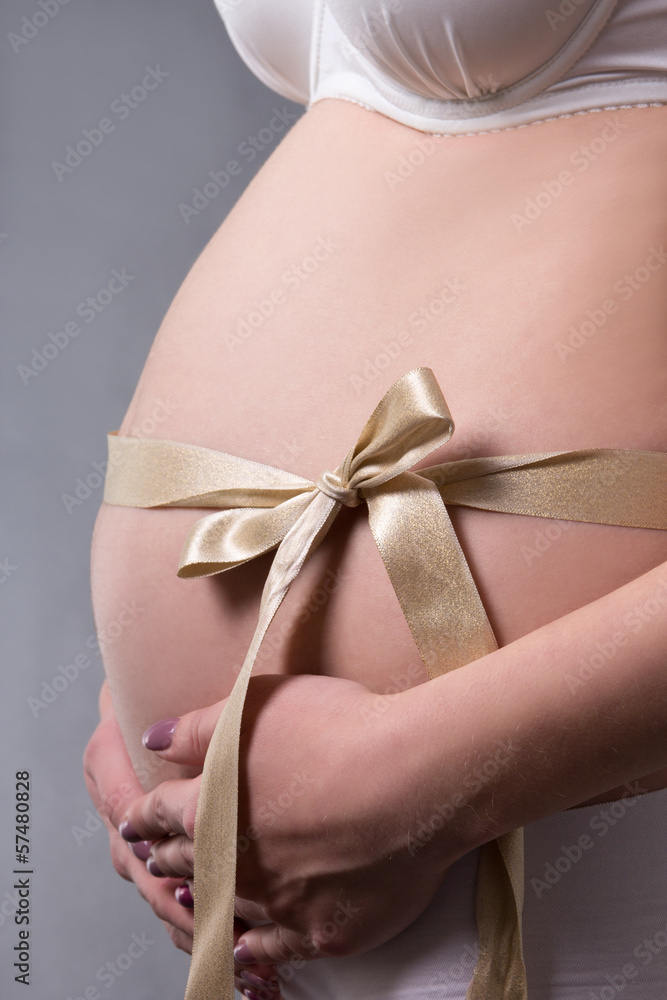 close up of pregnant belly with golden gift ribbon over grey close up of pregnant belly with golden gift ribbon over grey