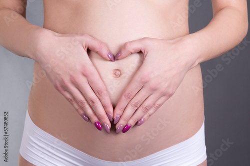 pregnant woman with hands in the shape of a heart over grey