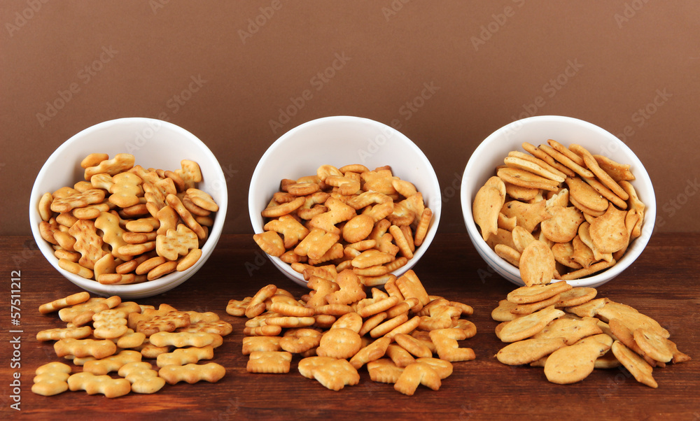 Delicious crackers in bowls on wooden table on brown background Delicious crackers in bowls on wooden table on brown background