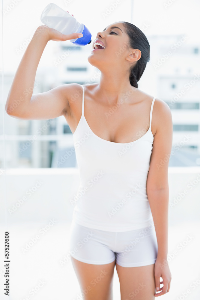 Happy toned brunette drinking from sports bottle Happy toned brunette drinking from sports bottle