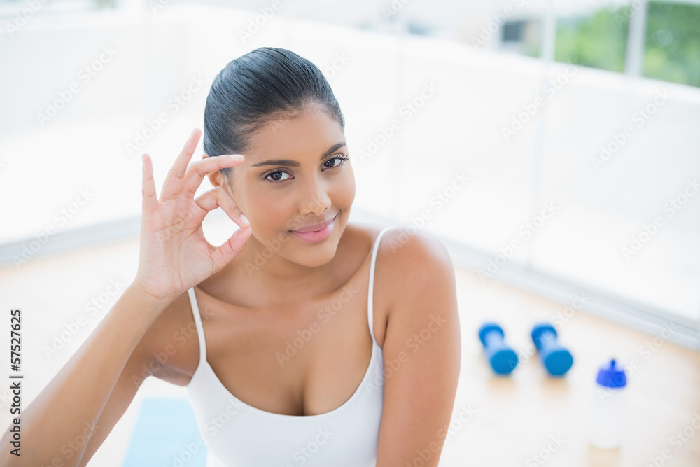 Happy toned brunette sitting on floor showing ok sign Happy toned brunette sitting on floor showing ok sign