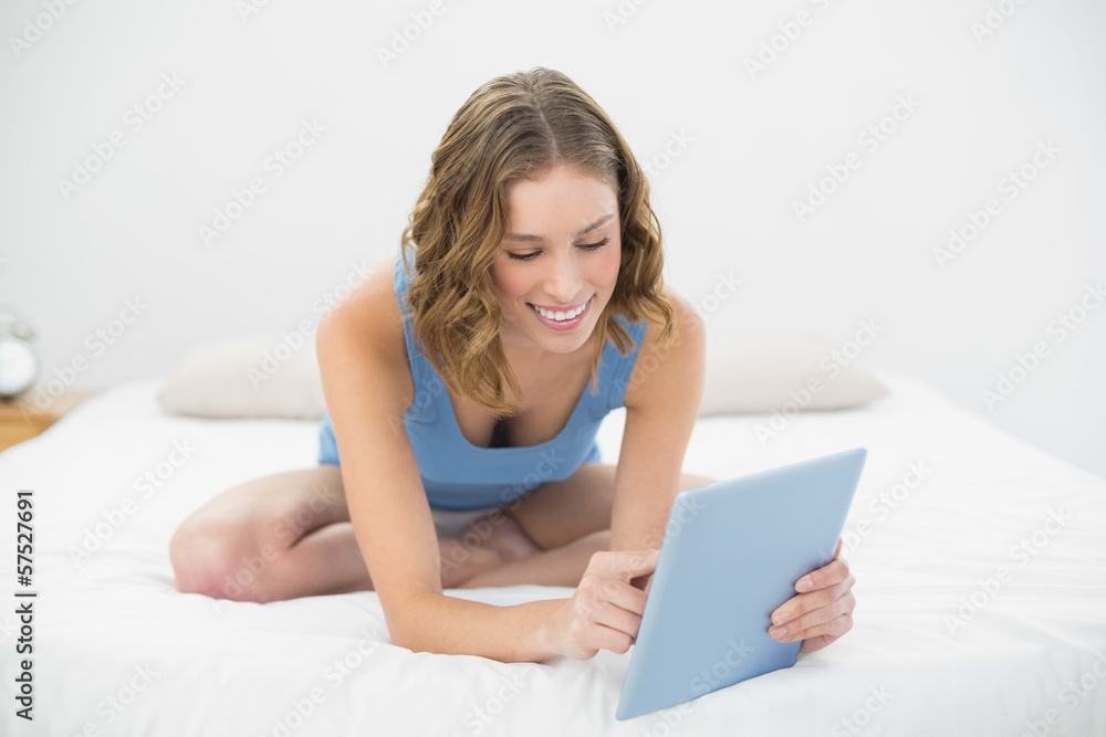 Lovely content woman sitting smiling on her bed using her tablet Lovely content woman sitting smiling on her bed using her tablet