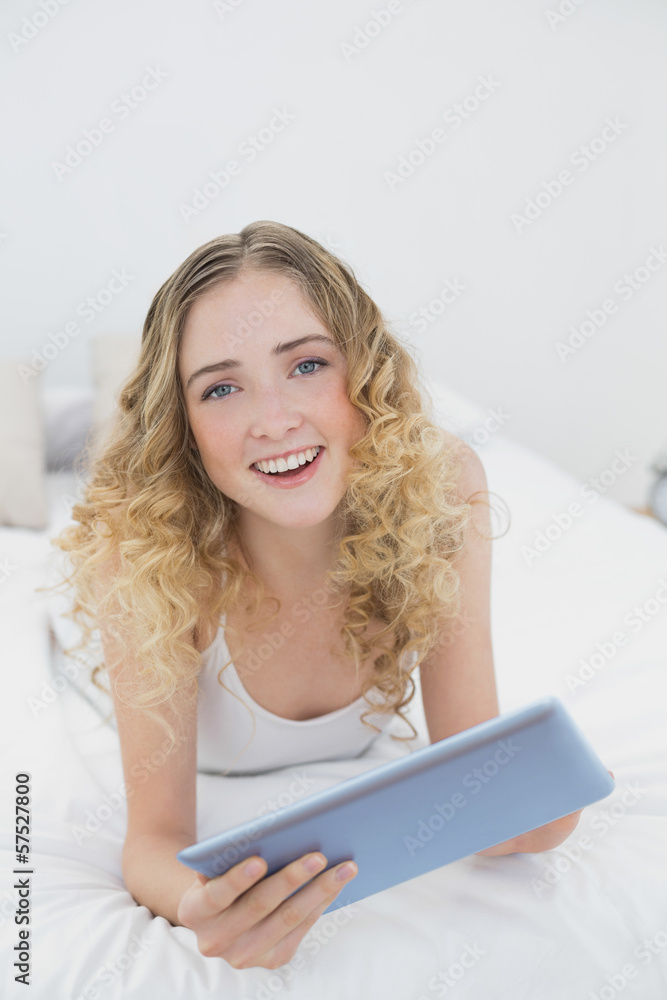 Pretty cheerful blonde lying on bed using tablet Pretty cheerful blonde lying on bed using tablet