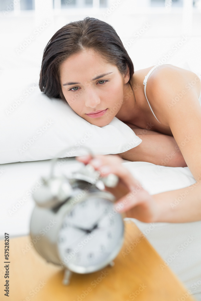 Woman in bed extending hand to alarm clock Woman in bed extending hand to alarm clock